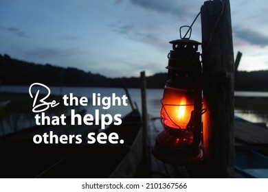 Inspirational Quote - Be The Light That Helps Others See. With Silhouette Of A Lantern Hanging On Wood In The Lake.