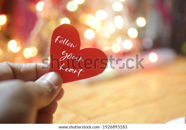 Inspirational quote - Follow you heart. With\
person holding red heart in hand against bright colorful bokeh\
light background. Love valentine, life purpose and believe in your\
heart intuition\
concept.