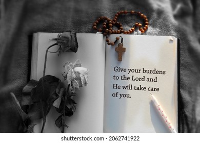 Inspirational quote - Give your burdens to the Lord and He will take care of you . With Wooden Rosary beads and Jesus Christ holy cross crucifix, dried wilted roses on the open book on the table.
