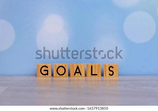 Inspirational quote - Goals. With single word on\
rustic wooden blocks  on soft blue bokeh background. Motivation\
word concept.