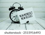 Inspirational quote New Mindset New Result text message with alarm clock on wooden background