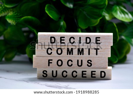 Inspirational words of decide commit focus succeed on wooden blocks with green background