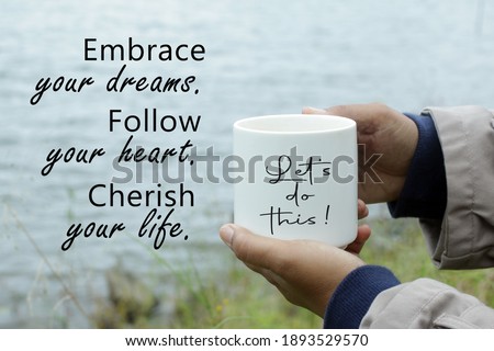 Inspirational words - Embrace your dreams. Follow your heart. Cherish your life. Lets do this. With person holding white cup of coffee or tea in hand on lake water background.
