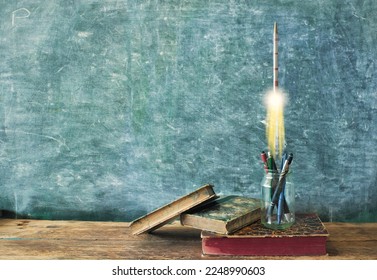 inspiration,education, knowledge and idea concept,books supplies and a rocketship launching in front of a blackboard, free copy space