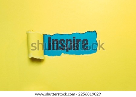 inspire word written with stamp letters, on blue paper seen thru ripped yellow paper strip