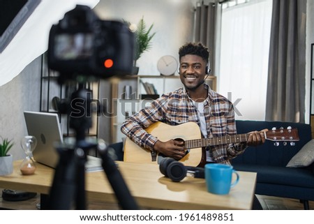 Inspired afro man playing guitar and recording music video for his social networks. Happu musician staying at home and using various modern gadgets.