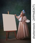 Inspired artist. Happy young woman in period attire standing with palette next to canvas and creating masterpiece, drawing against vintage green background. Concept of history, comparison of eras