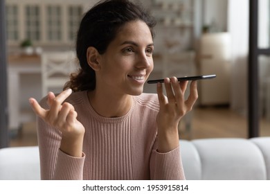 Inspired by innovations. Happy young hispanic woman sit on couch speak to phone ai give audio command search answer on question online. Confident millennial lady send vocal message using voicemail app