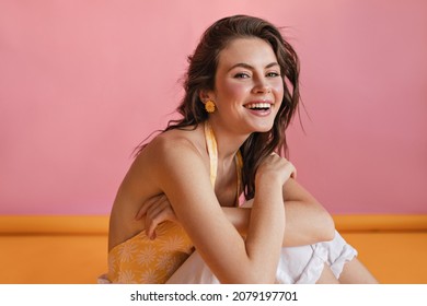 Inspired Caucasian Young Female Model Looking At Camera With Shy Smile Against Pink Wall. Photo Of Beautiful Brown-haired Woman In T-shirt, Relaxing At Photo Shoot.