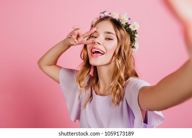 Inspired Fair-haired Girl In Purple Attire Spending Time In Studio. Close-up Portrait Of Lovable Blonde Lady In Flower Wreath Making Selfie And Laughing.