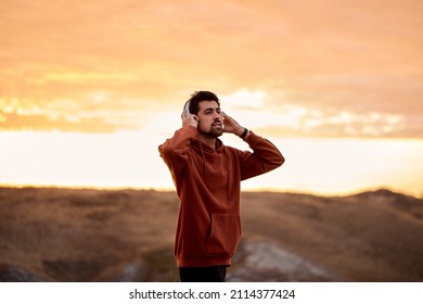 Inspired Handsome Guy Is Wearing Modern Wireless Headphones Headset Before Training, Sportive Fit Male Listen To Music On Jogging, In The Morning At Sunrise. Jogging, Run, Sport, Fitness Concept