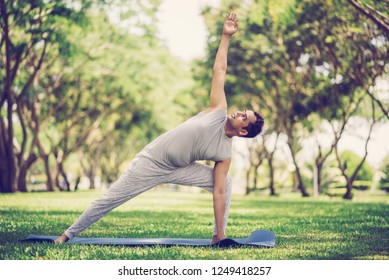 Inspired Indian Man Doing Yoga Asanas In City Park. Young Citizen Exercising Outside And Standing In Yoga Side Angle Pose. Fitness Outdoors And Life Balance Concept