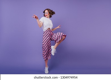 Inspired jocund girl in sneakers dancing on purple background. Gorgeous young female model with dark wavy hair jumping in studio. - Powered by Shutterstock