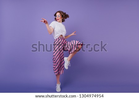 Inspired jocund girl in sneakers dancing on purple background. Gorgeous young female model with dark wavy hair jumping in studio.