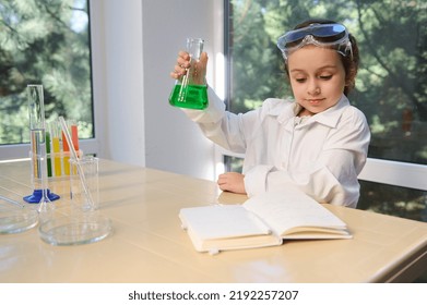 Inspired Little Girl, School Kid Wearing White Lab Coat And Safety Goggles, Testing Chemistry Lab Experiment And Shaking Glass Tube Flask, Looking At Chemistry Textbook. Science And Education