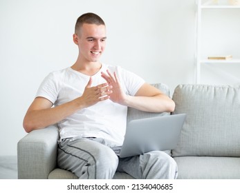 Inspired Meeting. Happy Man. Online Conference. Excited Casual Guy Sitting Sofa Looking Laptop Clapping Hands In Light Room Interior Copy Space.