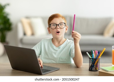 Inspired school kis redhead boy with glasses using laptop at home, raising hand with pencil up, smart preteen child showing eureka gesture, looking for creative solutions while studying, copy space