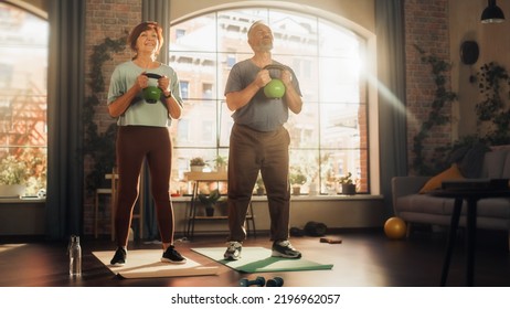 Inspired Senior Couple Doing Morning Exercises And Kettlebell Workout Together At Home In Bright Living Room. Concept Of Healthy Lifestyle, Fitness, Recreation, Couple Goals, Wellbeing And Retirement.