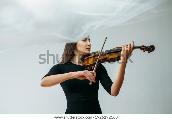Inspired
violinist woman. Online concert. Self isolation. Professional
artist. Calm lady playing violin closed eyes with transparent
plastic film under head isolated
neutral.