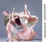 Inspired young, beautiful ballerina wearing rainbow dress dancing over grey studio background. Ballet with silk dress. Concept of classic ballet, inspiration, beauty, contemporary, dance, creativity