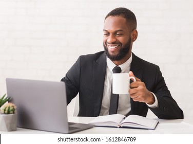 Inspired Young Black Entrepreneur Drinking Tea While Working With Laptop In Office, Copy Space