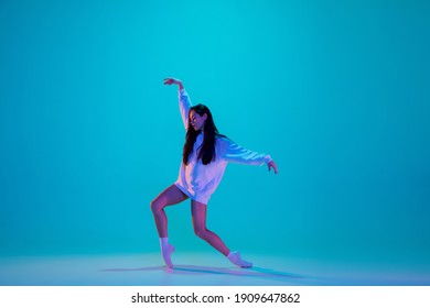 Inspired. Young and graceful ballet dancer isolated on blue studio background in neon light. Art, motion, action, flexibility, inspiration concept. Flexible caucasian ballet dancer, moves in glow.