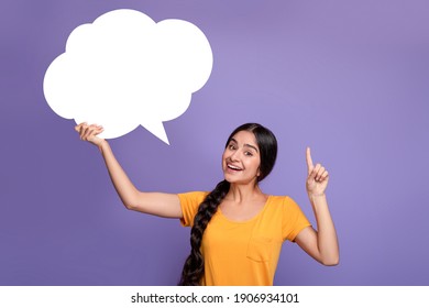 Inspired Young Indian Lady Having Idea, Holding Blank Speech Bubble And Pointing Finger Up, Showing Free Place For Your Text, Standing Over Purple Background In Studio, Copy Empty Space