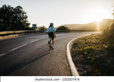 Inspiring Image Of Female Cyclist Ride Bicycle On Road Climb,golden Hour. Fit Sport Professional Woman Cycling At Mountain With Effort During Sunset. Athlete Riding Race. Achievement,success, Winning