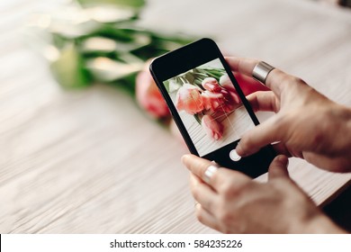 Instagram Photographer Blogging Workshop Concept. Hand Holding Phone And Taking Photo Of Stylish Flowers. Pink Tulips On White Wooden Rustic Background.space For Text. Hello Spring