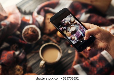 instagram photography blogging workshop concept. hand holding phone taking photo of stylish winter flat lay coffee cookies and spices on wooden rustic background. cozy mood autumn. - Powered by Shutterstock