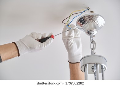 Installation ceiling lamp, hands of male electrician fixing chandelier with use of professional tools
