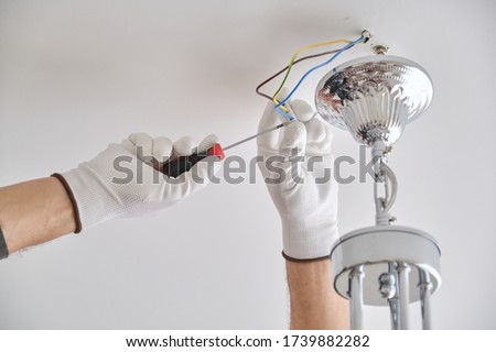 Installation ceiling lamp, hands of male electrician fixing chandelier with use of professional tools