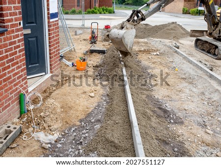 Installation of edging kerb during footpath construction in front of new build house on new housing  development and placing semidry concrete around it with excavator.