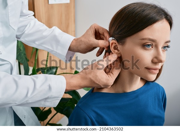 Installation\
hearing aid on woman\'s ear at hearing clinic, close-up, side view.\
Deafness treatment, hearing\
solutions