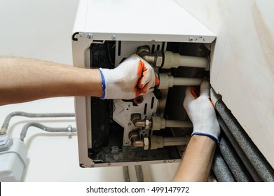 Installation Of Home Heating. A Worker Attaches The Pipe To The Gas Boiler.