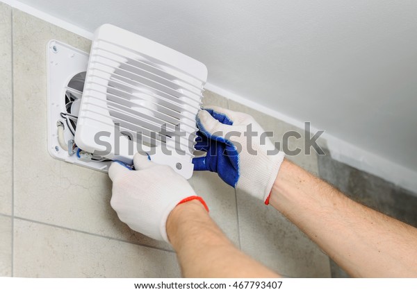 Installation of household appliances. Workman
fixing the exhaust fan on the
wall.