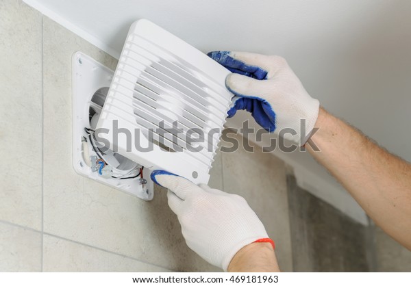 Installation of household appliances. Workman\
fixing the exhaust fan on the\
wall.
