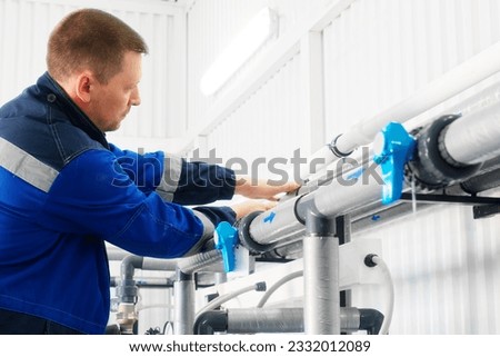 Installation of industrial water treatment system. Man in overalls is adjusting indoor water supply system. Plumber diagnoses pipes. Authentic workflow.