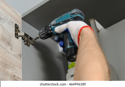 Installation of kitchen. Workman fixes  a hinge to a kitchen cabinet. - Shutterstock ID 464996189
