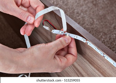 Installation Of LED Strip Light For Decorative Lighting Of Furniture, Close-up Hands Of Electrician.