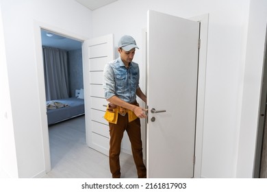 Installation Of A Lock On The Front Wooden Entrance Door. Portrait Of Young Locksmith Workman In Blue Uniform Installing Door Knob. Professional Repair Service. Maintenance Concept