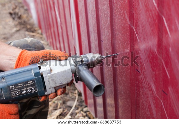 Installation of metal fence. Man drilling a hole\
in the metal\
fence.