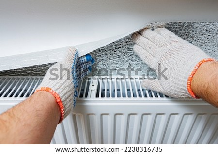 Installation of a polythene film of aluminum multi-foil thermal insulation on the wall behind the heating radiator at home. Thermal insulation of the apartment, to save money on utilities, heating