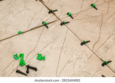 Installation process of marble pattern ceramic floor tiles using plastic tile leveling system clips and wedges. Green clips and black wedges secure even gaps between slabs during renovation work.