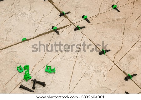 Installation process of marble pattern ceramic floor tiles using plastic tile leveling system clips and wedges. Green clips and black wedges secure even gaps between slabs during renovation work.