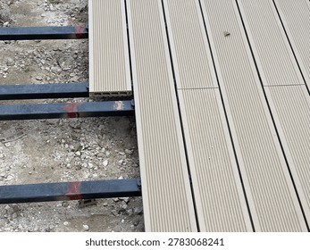 Installation process of wood plastic composite decking boards on metal joists frame, outdoor terrace patio construction with grooved WPC planks, carpentry floor renovation context over gravel ground