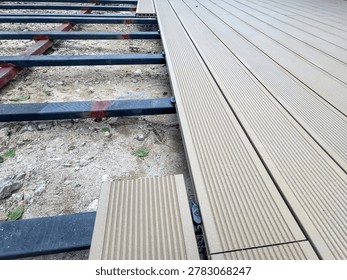 Installation process of wood plastic composite decking boards on metal joists frame, outdoor terrace patio construction with grooved WPC planks, carpentry floor renovation context over gravel ground