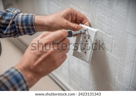 Installation or repair of electrical outlet socket box within the wall. Hands of serviceman or repairman fixing with Type B Duplex Receptacle - American socket with grounding 