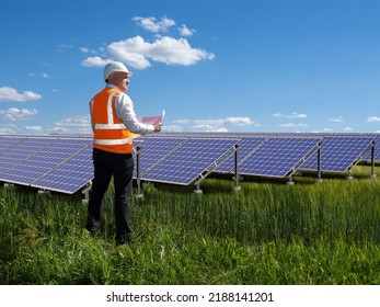 Installation Of Solar Panels. Energy Company Employee. Man In Orange Vest In Front Solar Panels. Concept Services For Installation Of Solar Panels. Engineer Oversees Operation Of Sun Power Plant