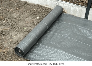 Installation of weed control fabric over soil before gravel placement, showing landscaping preparation and ground protection. Side view.